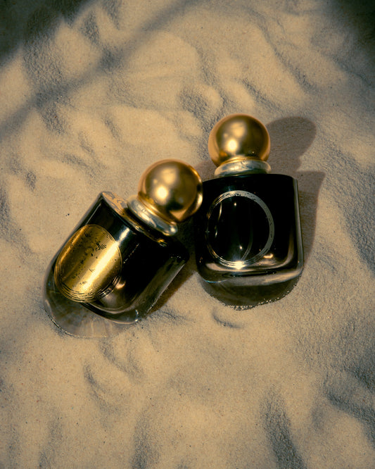  Sage and Salt perfumes Moon Ring and Luna Absolute displayed on sunlit sand, showcasing luxury black bottles with gold caps—ritual fragrances inspired by lunar phases.